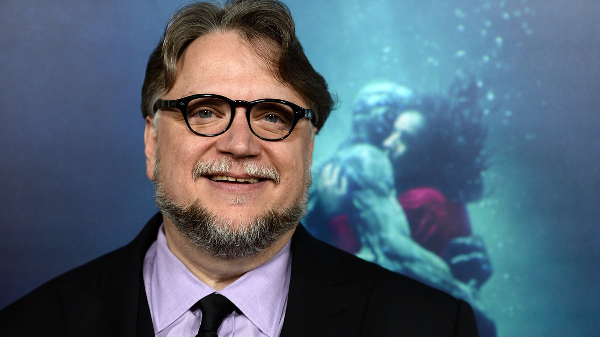 SHAPE OF WATER – DAS FLÜSTERN DES WASSERS: Regisseur Guillermo del Toro steht vor einer Röhre, in der ein mysteriöses Wesen und eine Frau sich im Wasser umarmen.