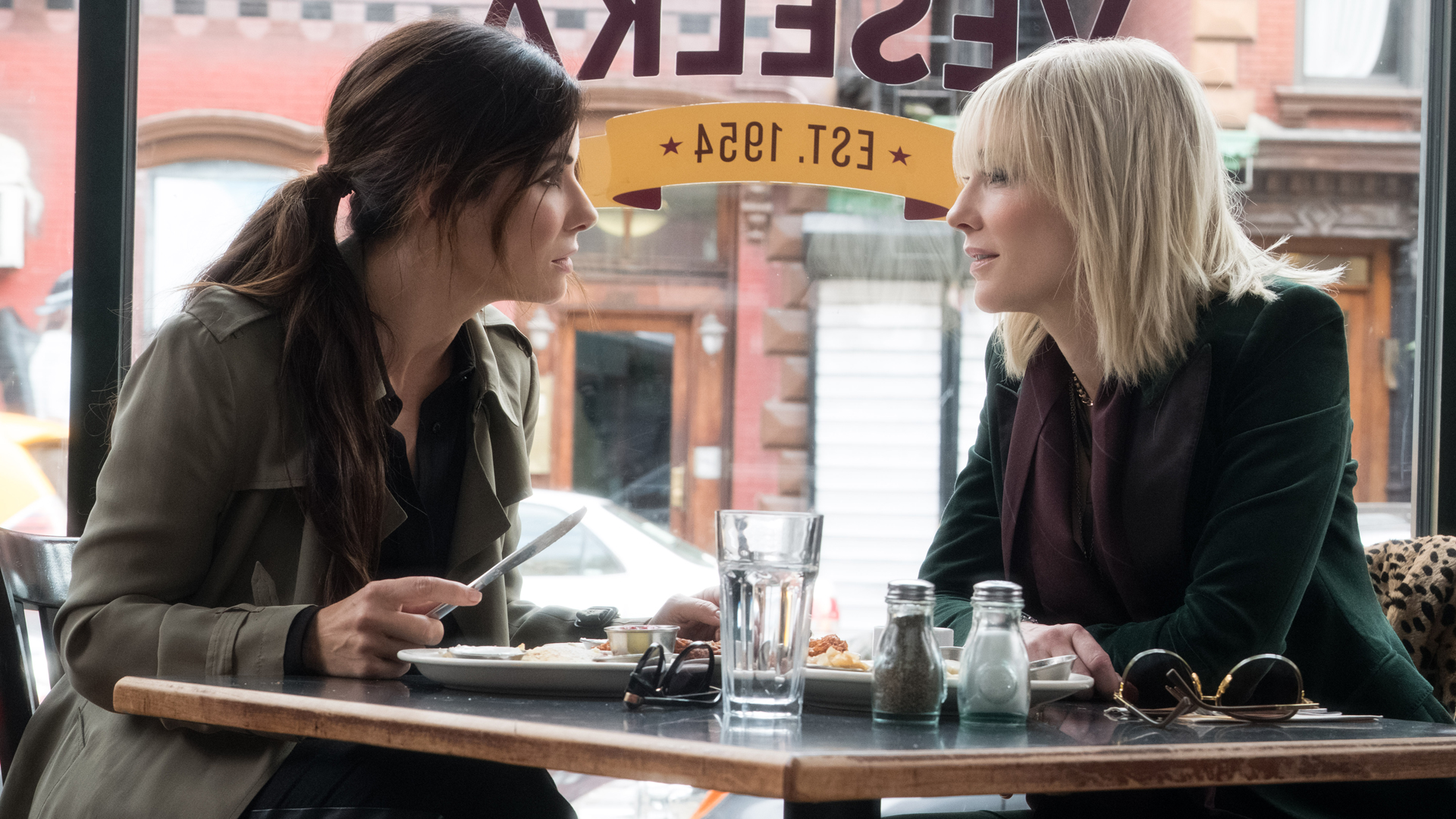 OCEAN’S 8: Sandra Bullock und Cate Blanchett sitzen an einem Tisch und hecken einen Plan aus.