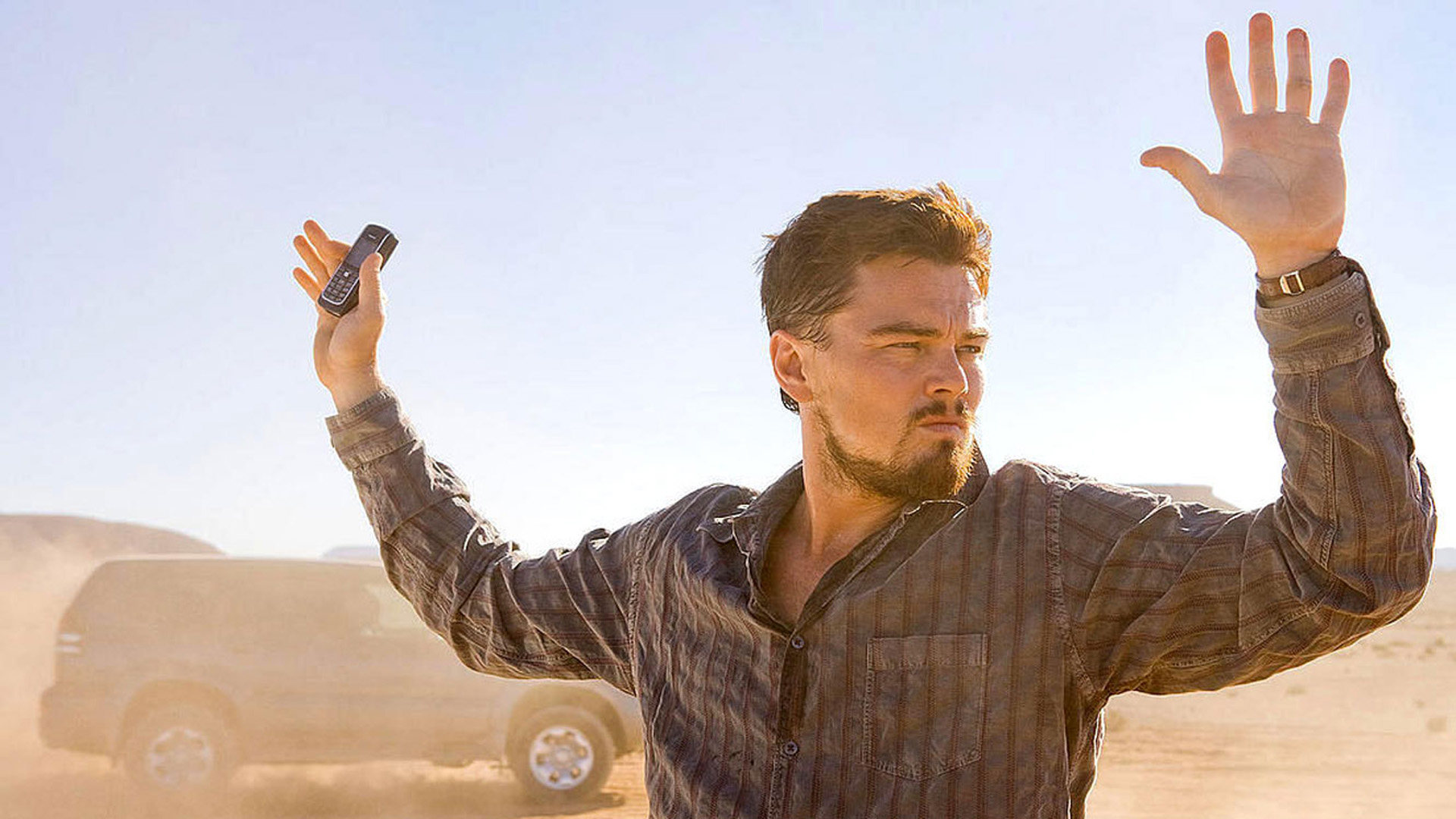 DER MANN, DER NIEMALS LEBTE: Leonardo diCaprio steht in einer staubigen, sonnendurchfluteten Wüstenlandschaft. Er ergibt sich und hält beide Hände in die Höhe.