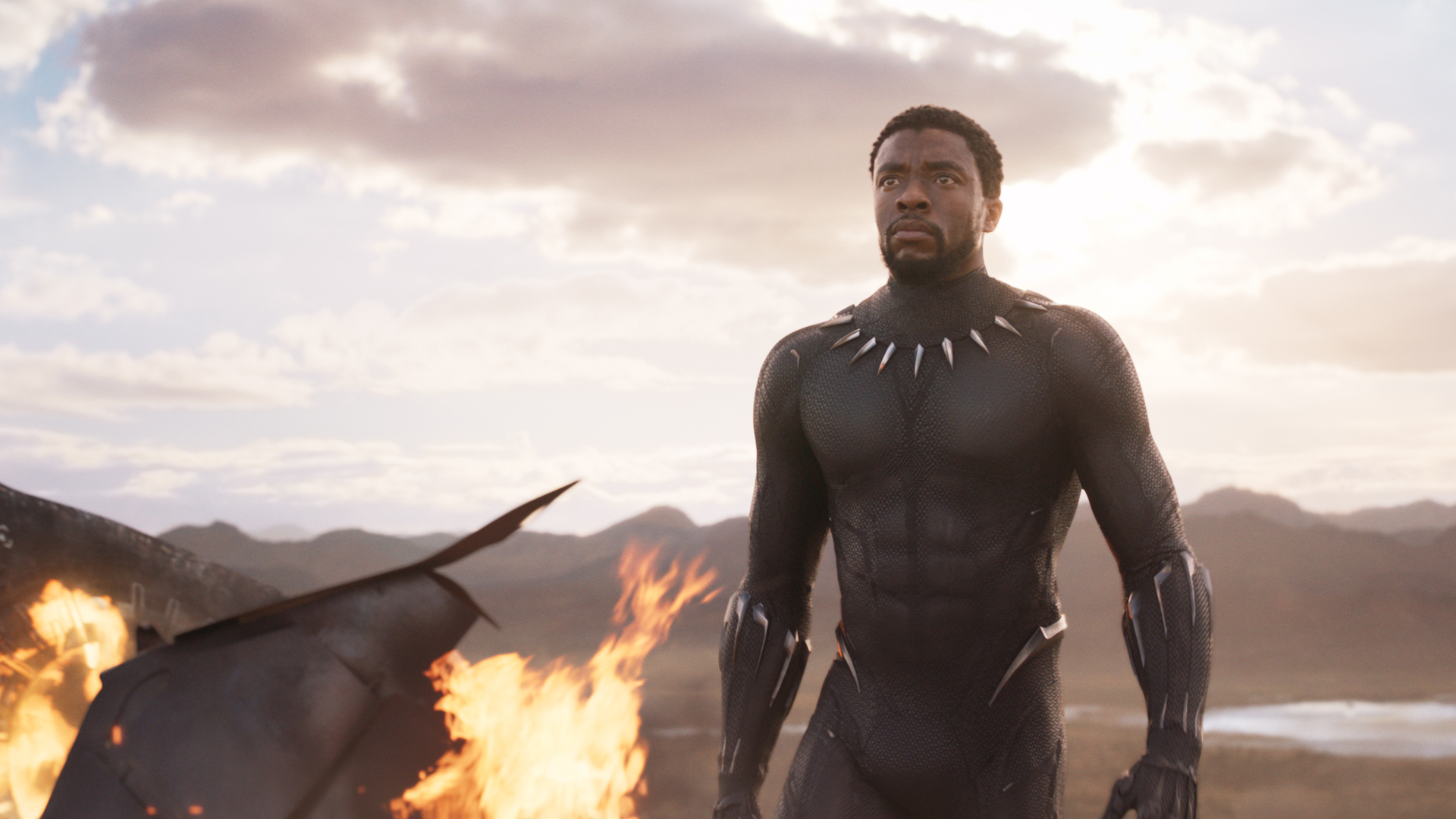 BLACK PANTHER: Black Panther steht in einer Bergregion und schaut gen Himmel. Neben ihm brennt ein Feuer.