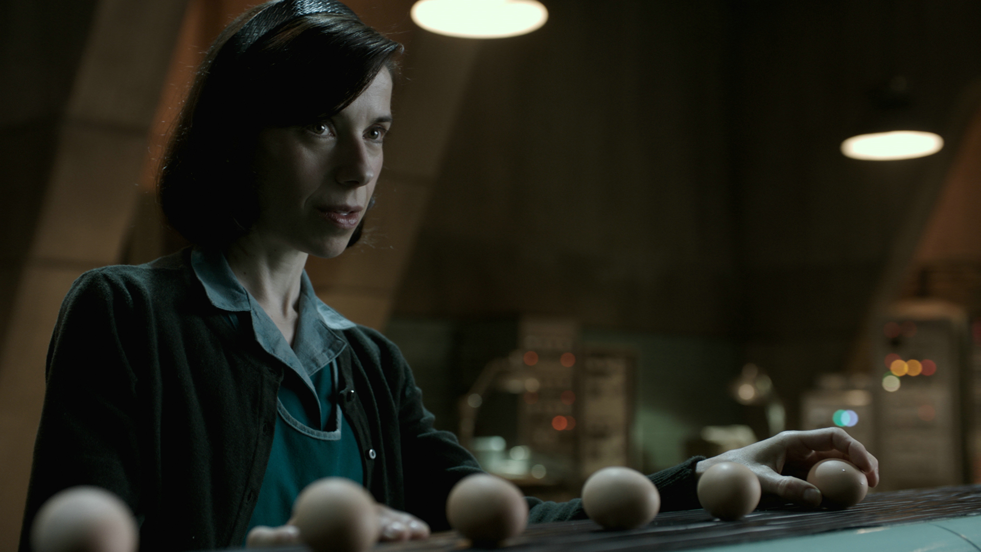 SHAPE OF WATER – DAS FLÜSTERN DES WASSERS: Elisa (Sally Hawkins) steht vor einem spärlich beleuchteten Hintergrund und hält ein Ei in der Hand.