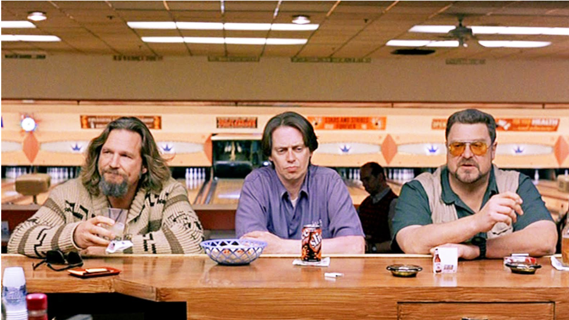 the big lebowski: Der Dude sitzt mit seinen Freunden an der Bar. Im Hintergrund eine Bowlingbahn