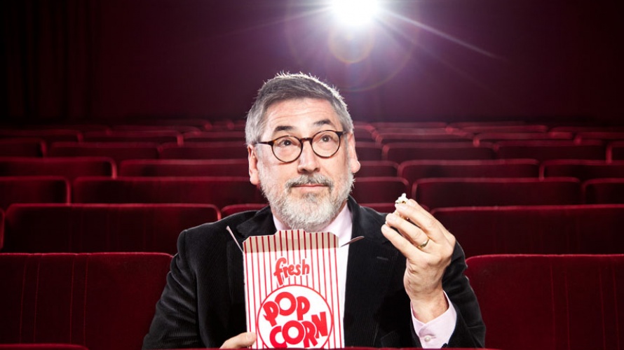 John Landis sitzt in einem leeren Kino und isst Popcorn.