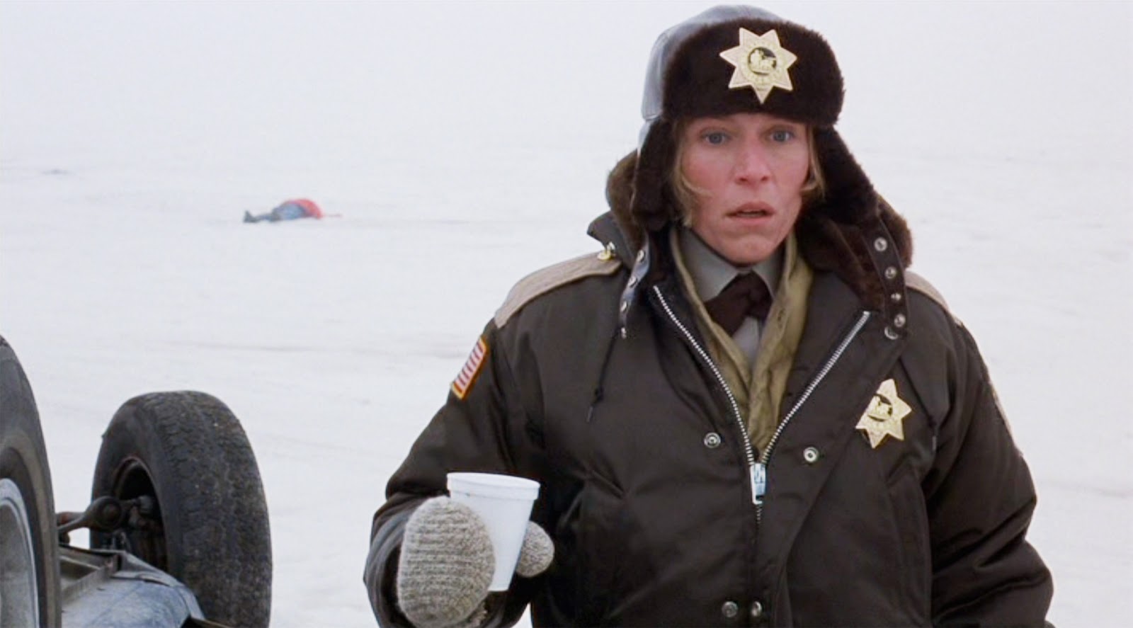 FARGO – BLUTIGER SCHNEE: Polizistin Marge Gunderson (Frances McDormand) steht in einer verschneiten Landschaft und schaut erschrocken. Hinter ihr liegt eine Leiche.