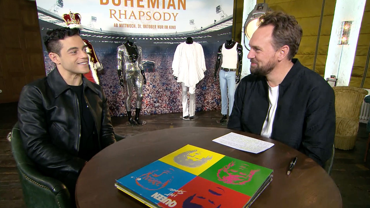 Rami Malek (Freddie Mercury) und Steven Gätjen sitzen an einem Tisch und sprechen über BOHEMIAN RHAPSODY.