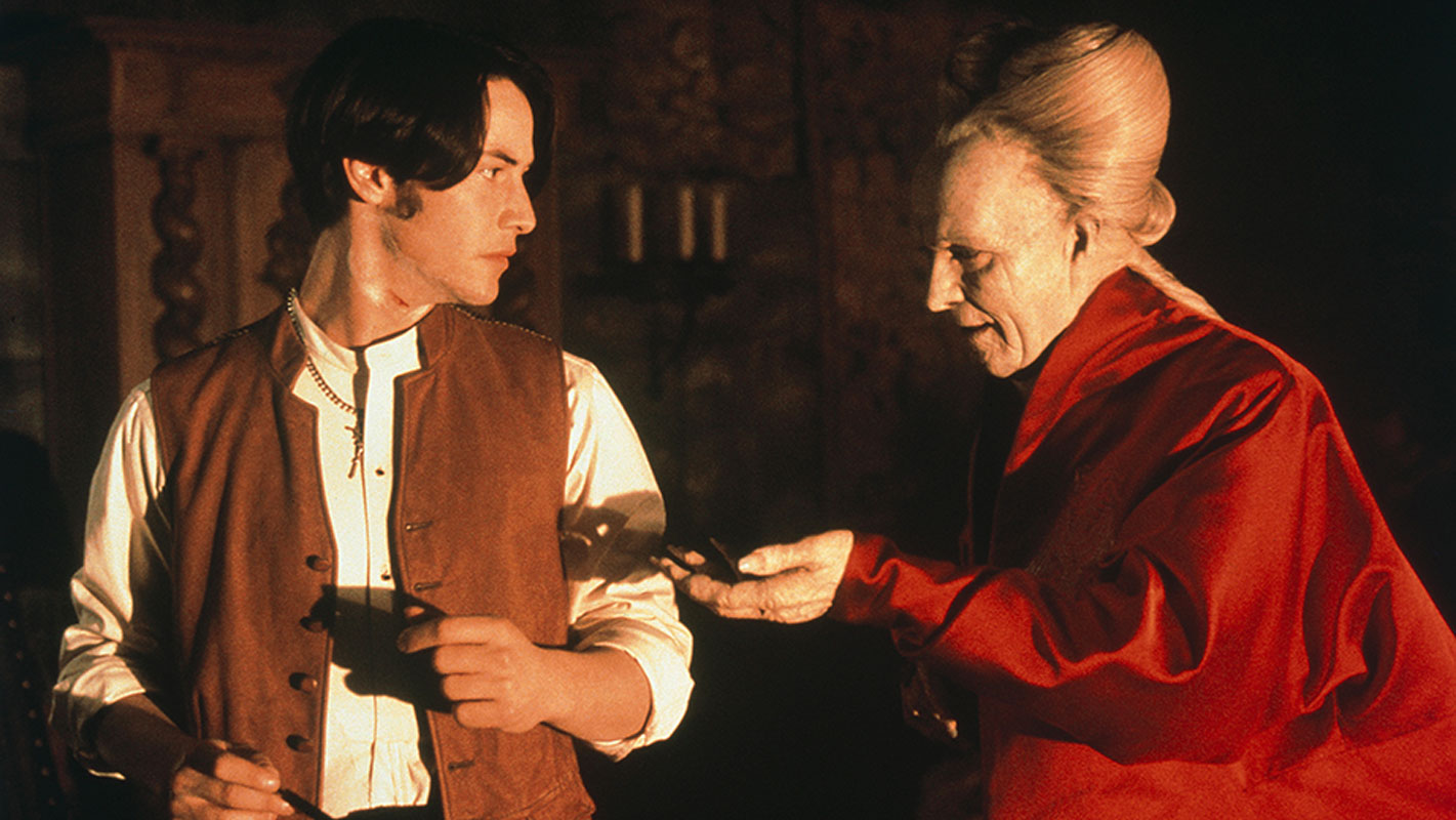 BRAM STOKER’S DRACULA: Jonathan Harker (Keanu Reeves, links) und Dracula (Gary Oldman, rechts) stehen in einem spärlich beleuchteten Raum eines Schlosses. Dracula trägt einen roten Samtmantel und streckt Harker die linke Hand entgegen, als wolle er ihm etwas anbieten. Harker trägt eine Weste und schaut skeptisch.