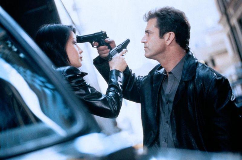 Für 70.000 Dollar geht Mel Gibson im Thriller PAYBACK – ZAHLTAG über Leichen und legt sich mit einem mächtigen Verbrechersyndikat an. Im Szenenfoto richtet er eine Pistole auf Lucy Liu – und sie eine auf ihn.