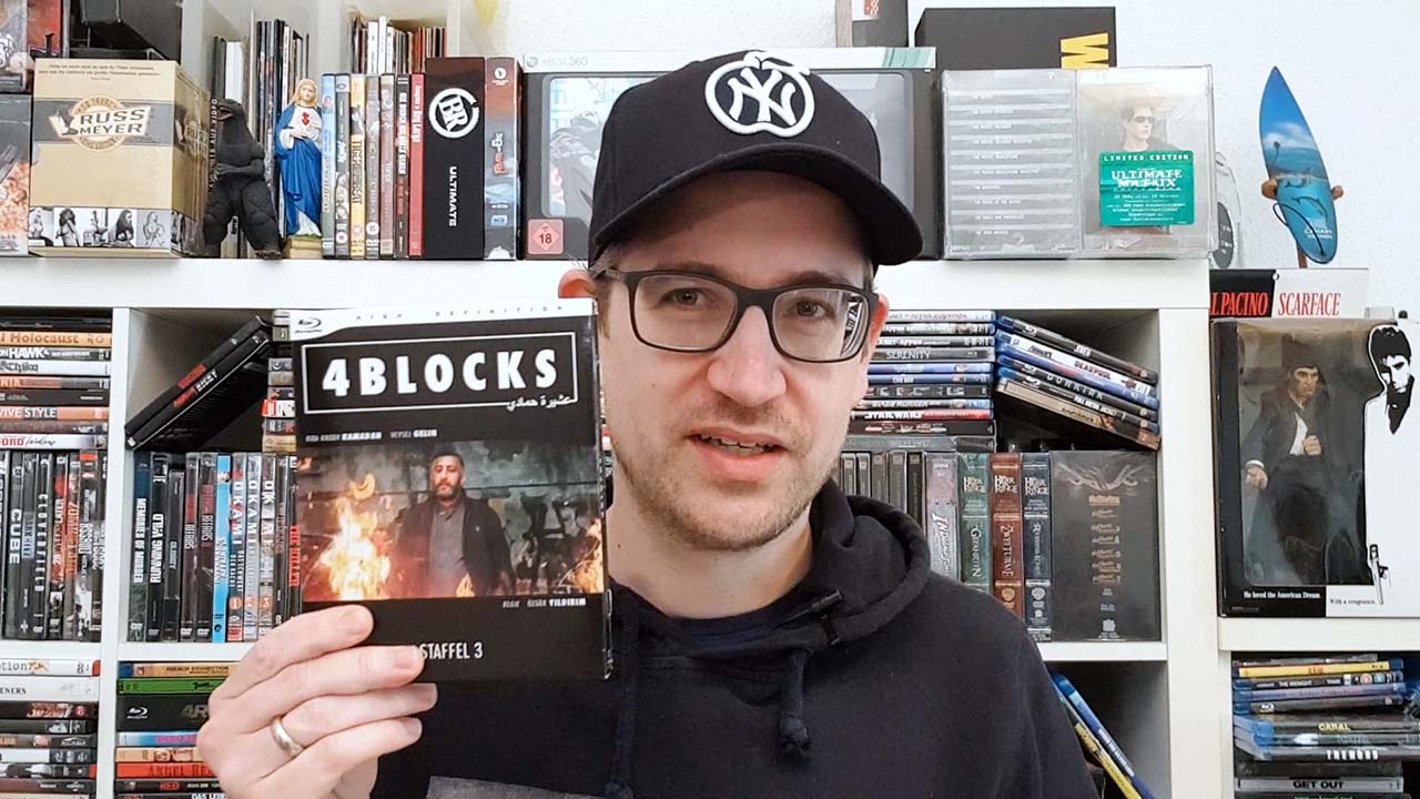 4 BLOCKS – Staffel 3: Daniel Schröckert steht vor seiner Filmsammlung und hält die Blu-ray der Serie in der rechten Hand